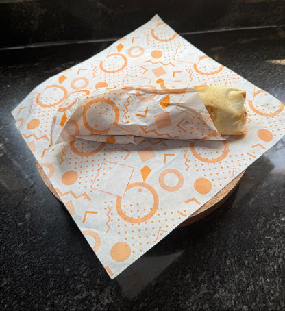 Burrito / Shawarma wrapped in orange grease paper on a patterned napkin 